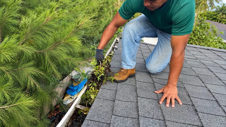 Technician clearing debris from a residential roof gutter in Oahu